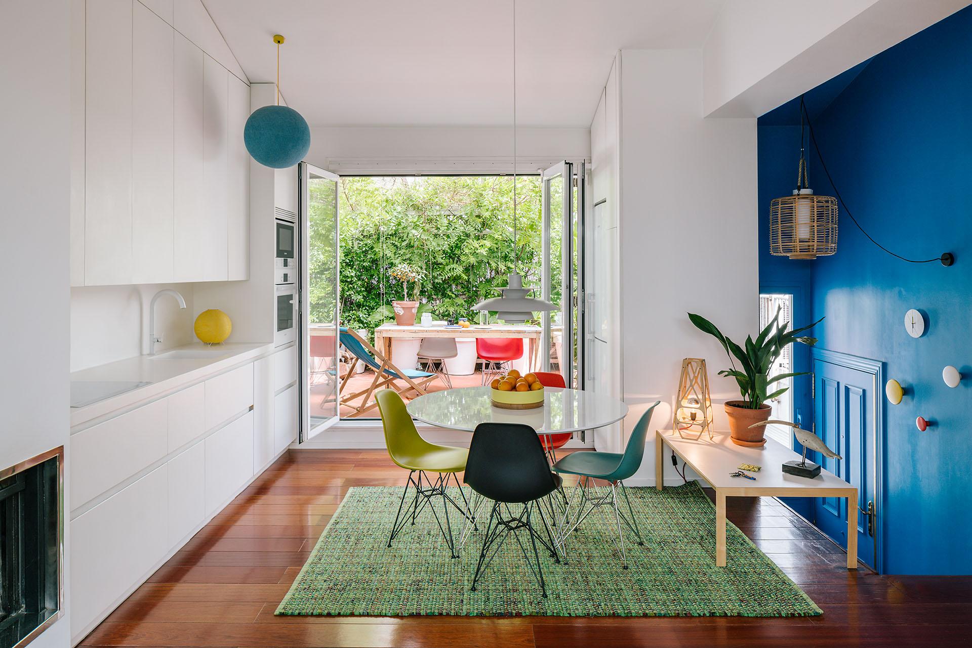 Bright modern dining area featuring a round table, colorful chairs, and open doors leading to an outdoor space.
