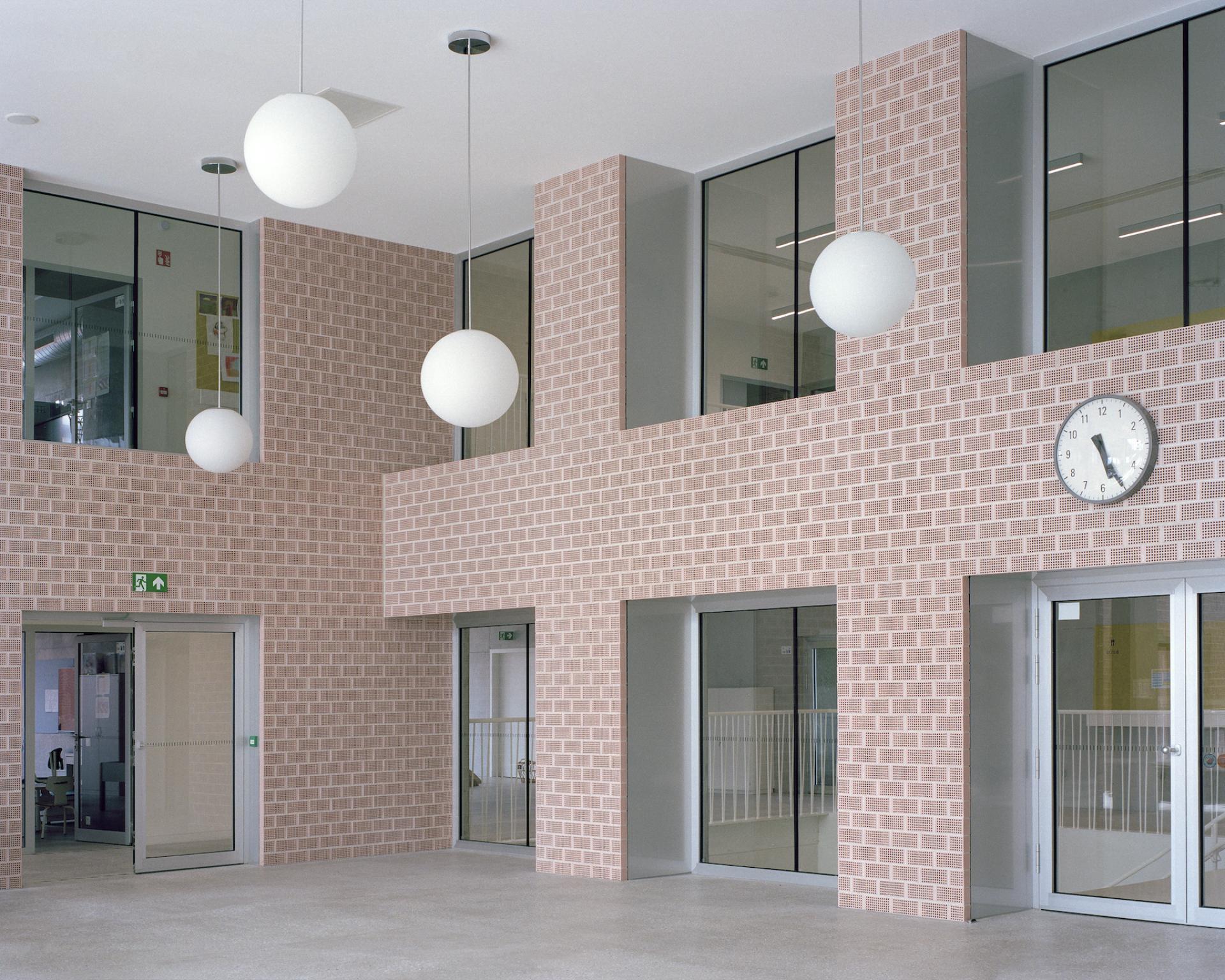 Modern interior of a multipurpose school featuring exposed brick walls, glass doors, and suspended lighting fixtures.