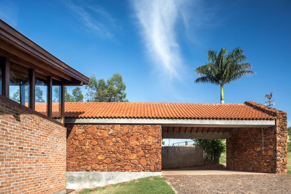 Modern architecture of The Lake House in Brazil, showcasing natural stone walls and a terracotta roof under a blue sky.