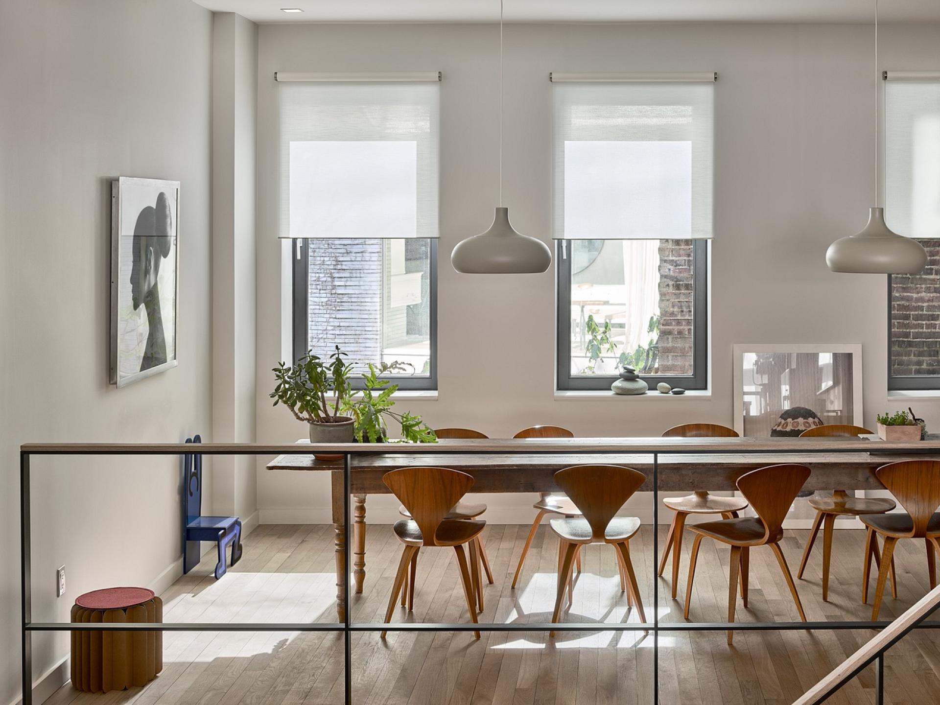 Brightly lit modern dining area featuring wooden chairs, a long table, and large windows with natural light.