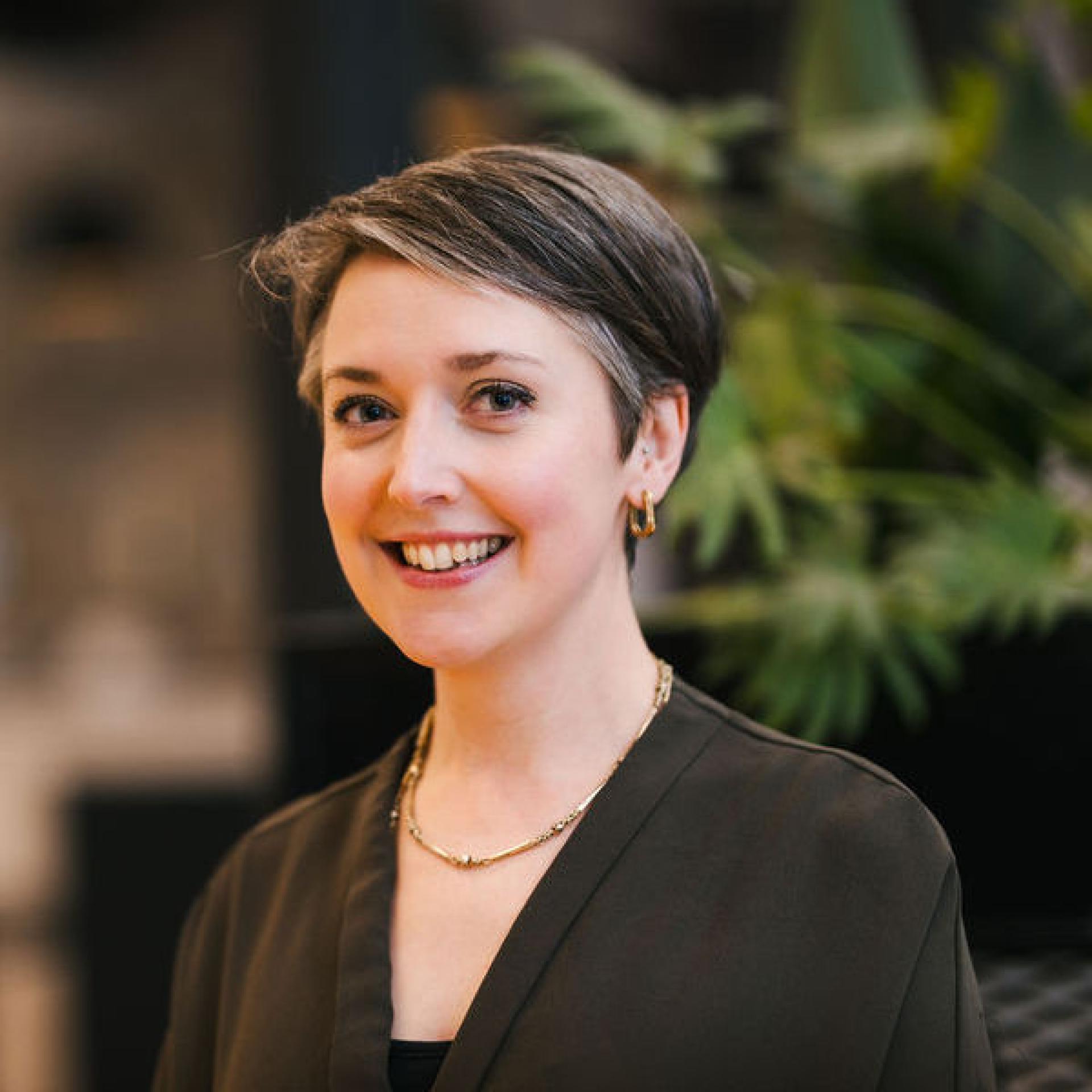 Professional woman smiling in front of decorative plants, representing insights on Glasgow's property outlook and market trends.