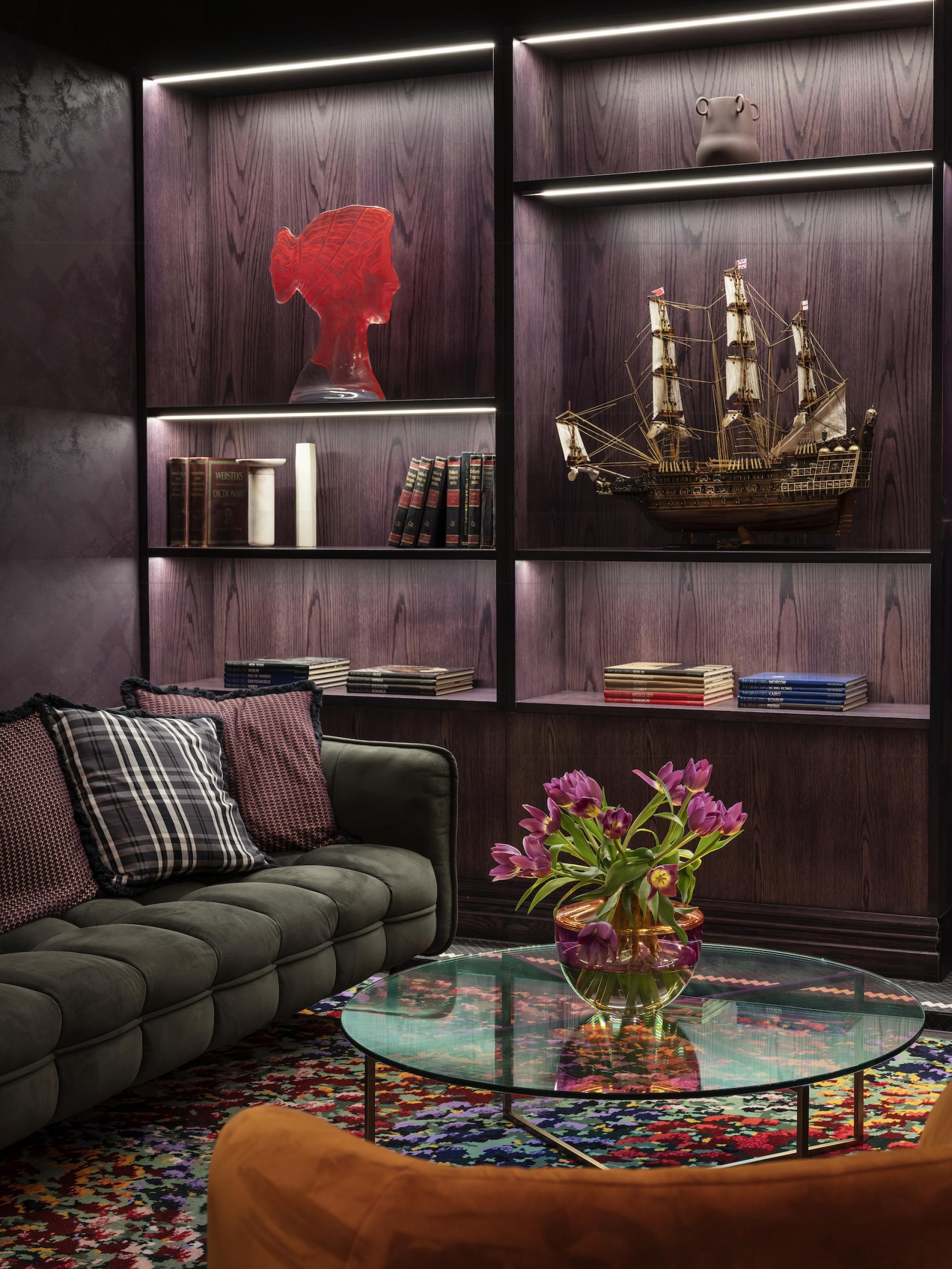 Eclectic interior featuring a green sofa, colorful rug, and artistic decor including a red sculpture and vintage books.