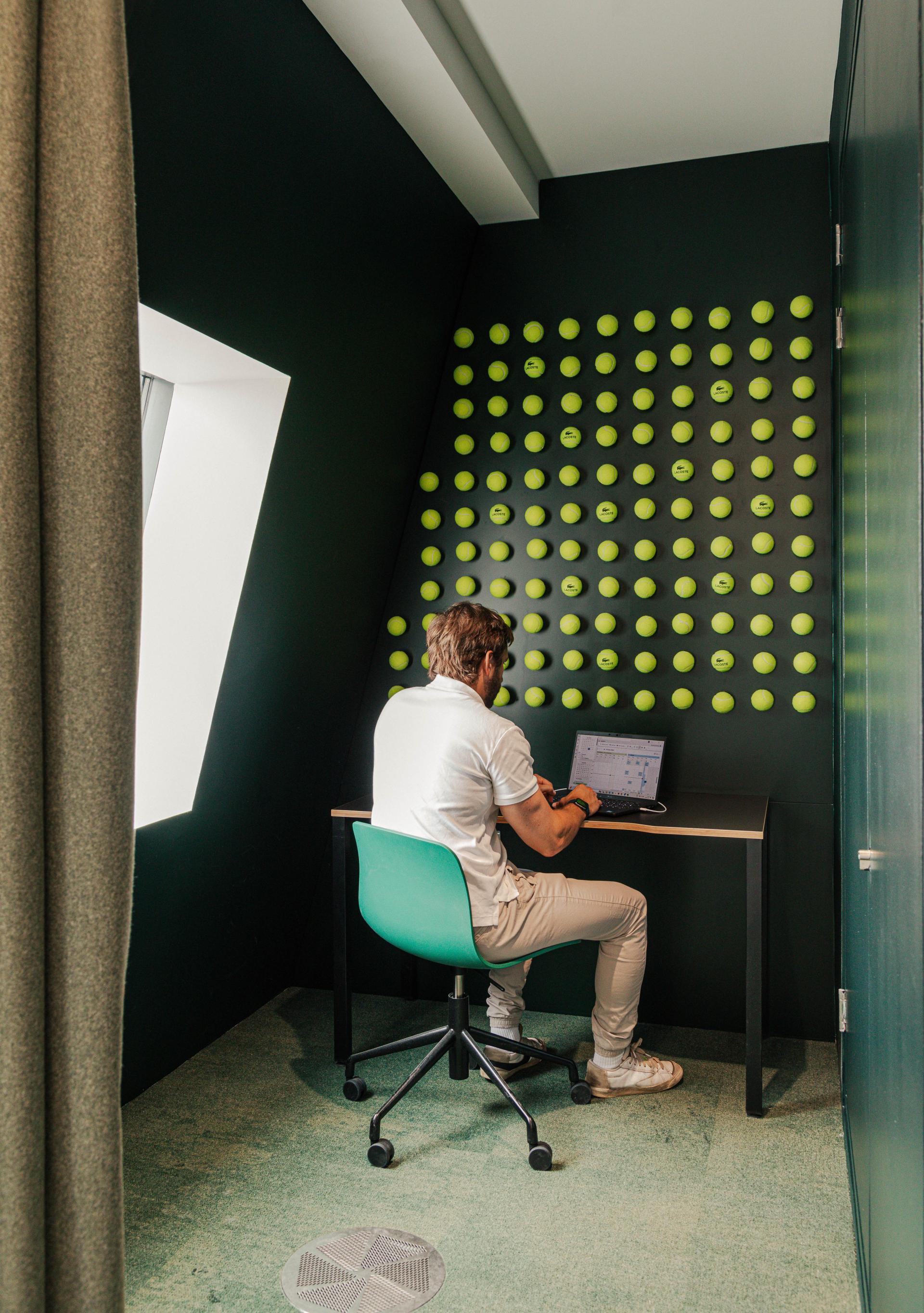 Innovative workspace design for Lacoste, featuring a unique green tennis ball wall and modern desk setup.