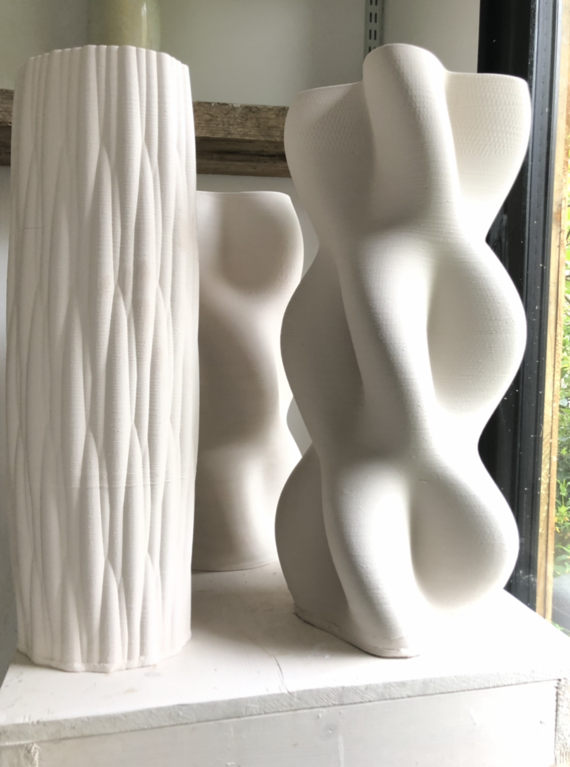 Three white ceramic sculptures with textured and abstract forms displayed on a shelf, highlighting innovative design in pottery.