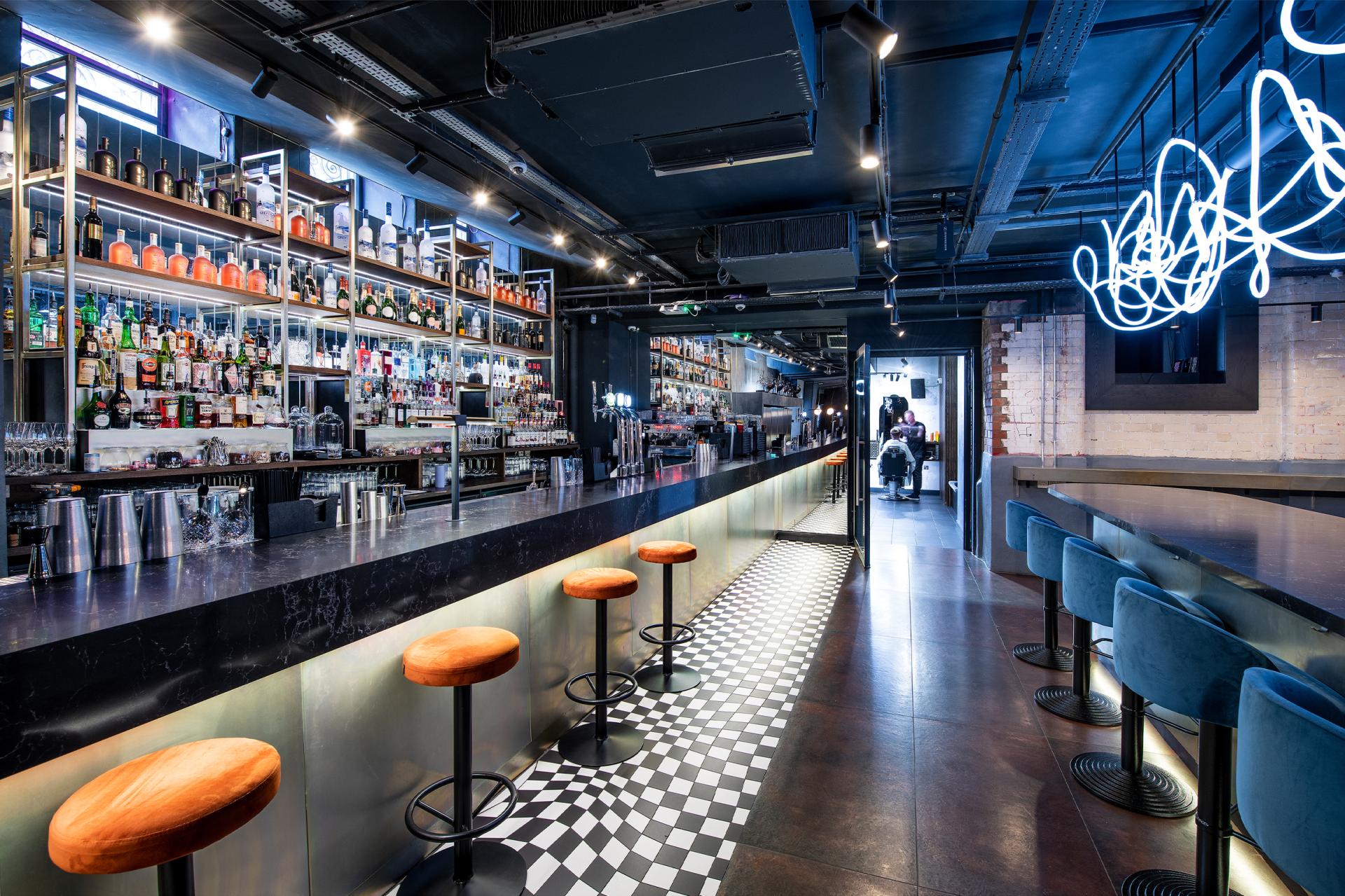 Stylish bar interior featuring wooden stools, illuminated shelves of spirits, and contemporary design elements, reflecting modern hospitality.