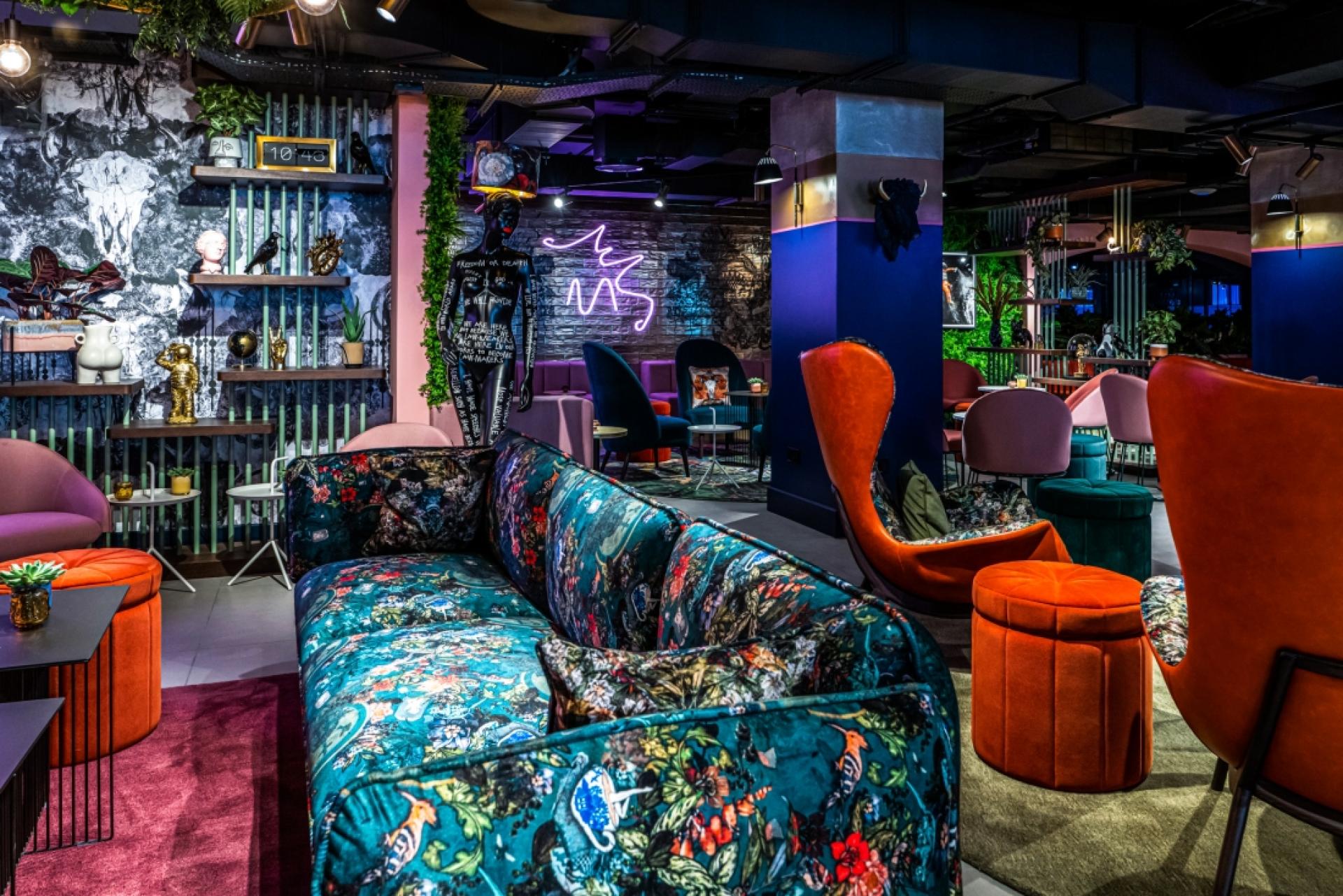 Vibrant hospitality interior featuring a floral sofa, artistic decor, neon lights, and eclectic seating arrangements.