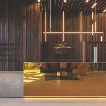 Modern office reception area featuring a sleek golden desk, wooden walls, and contemporary lighting design.