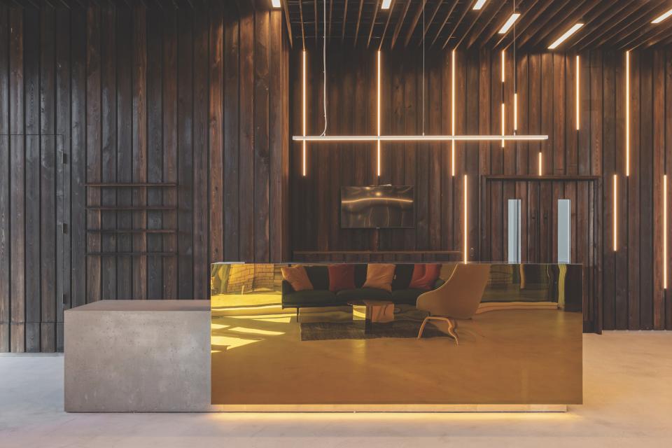 Modern office reception area featuring a sleek golden desk, wooden walls, and contemporary lighting design.