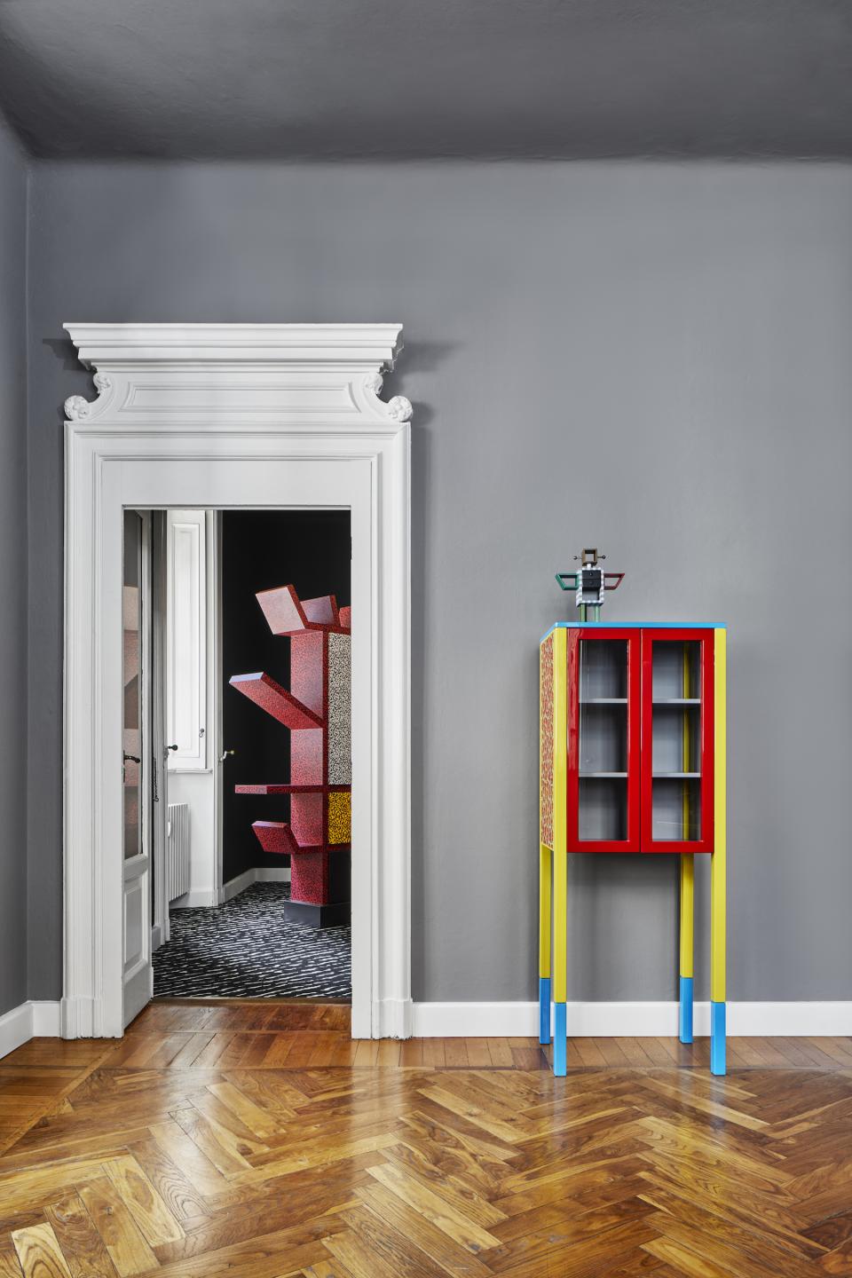 Colorful Memphis Milano furniture stands against a grey wall, showcasing a vibrant design aesthetic in a stylish interior setting.