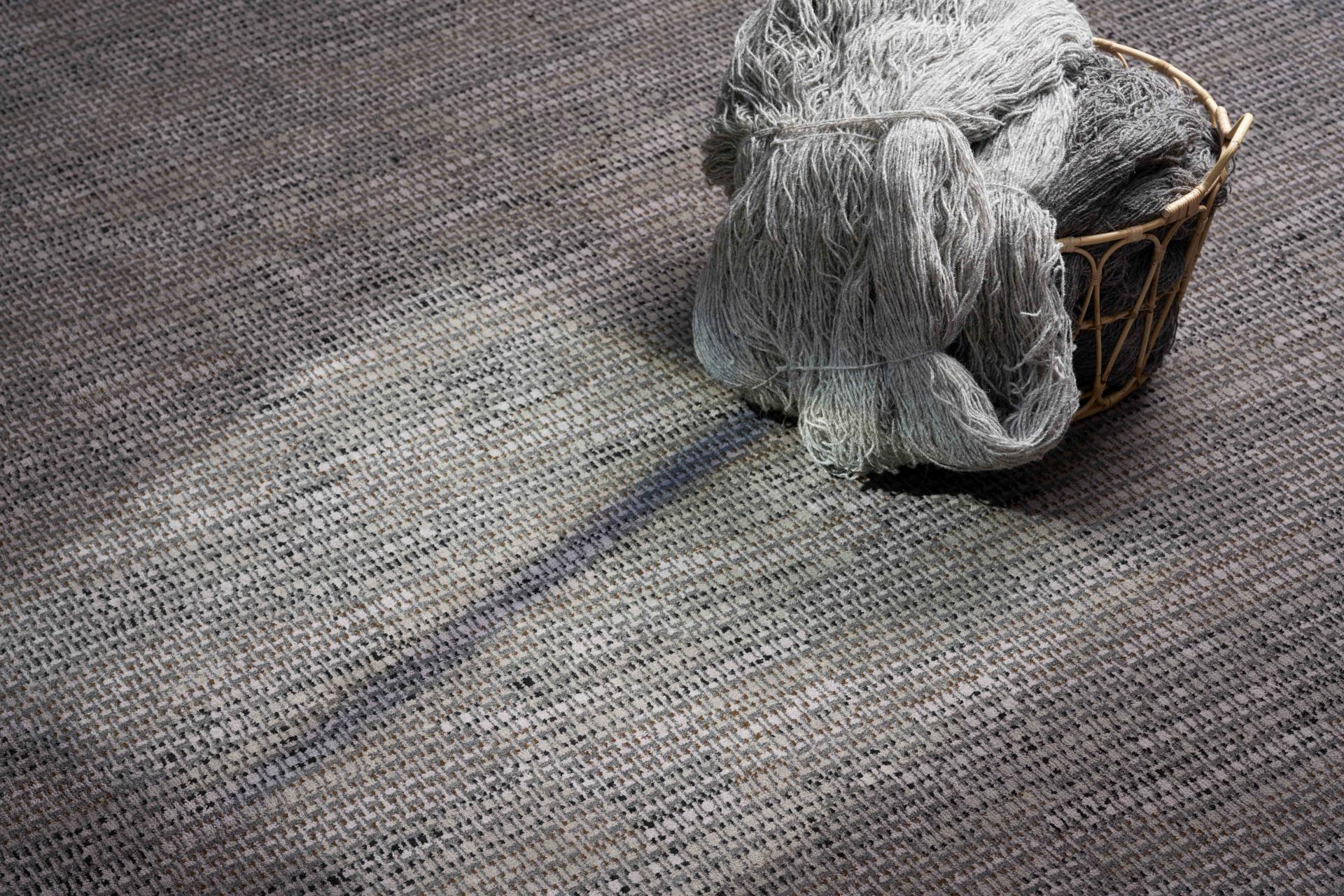 Textured gray macrame yarn bundled in a woven basket, set against a patterned carpet background, highlighting the Macrame Collection by Newhey Carpets.