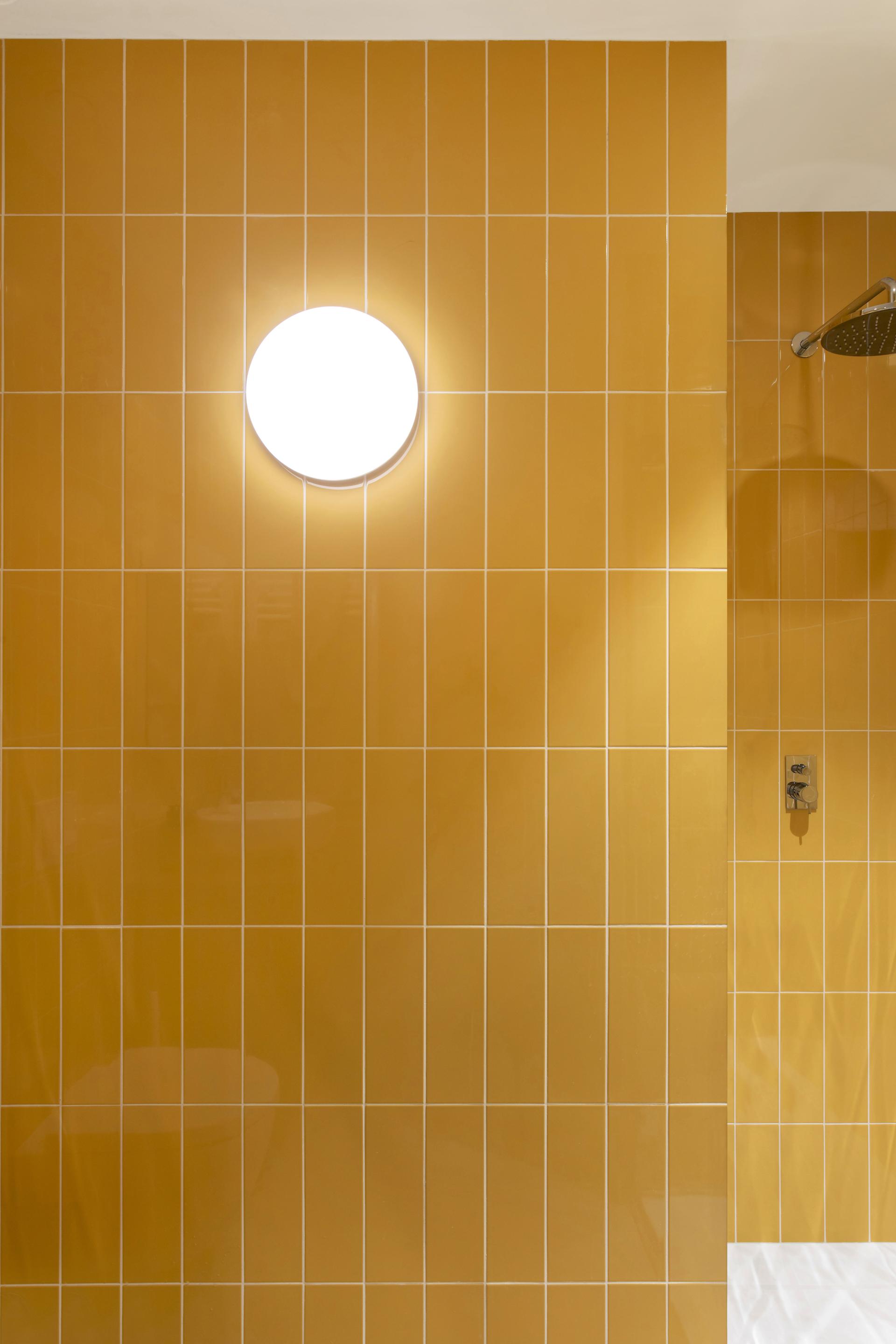 Bright yellow ceramic tiles adorn a bathroom wall, enhanced by a round lighting fixture for modern design.