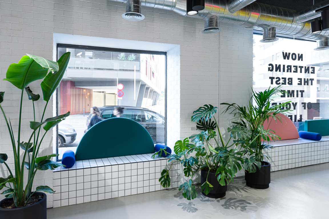 Bright, modern co-working space at The Student Hotel in Barcelona, featuring vibrant seating and indoor greenery.