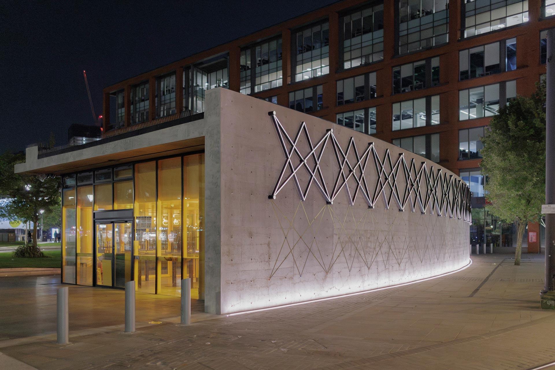 Modern Piccadilly Gardens Pavilion in Manchester, showcasing unique architectural design and illuminated exterior at night.