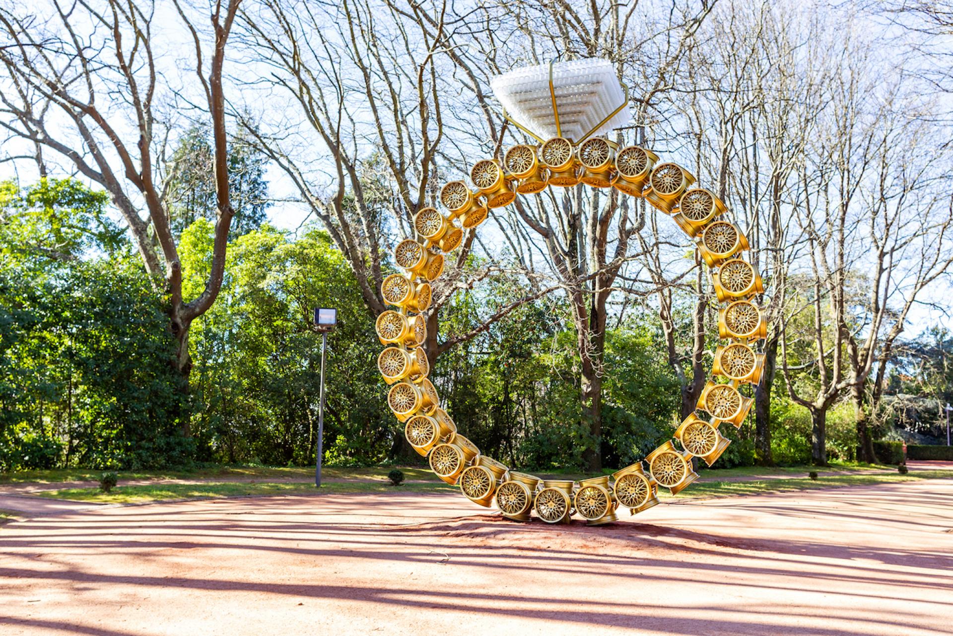 Large golden ring sculpture surrounded by trees at Yorkshire Sculpture Park, showcasing Joana Vasconcelos' art installation.