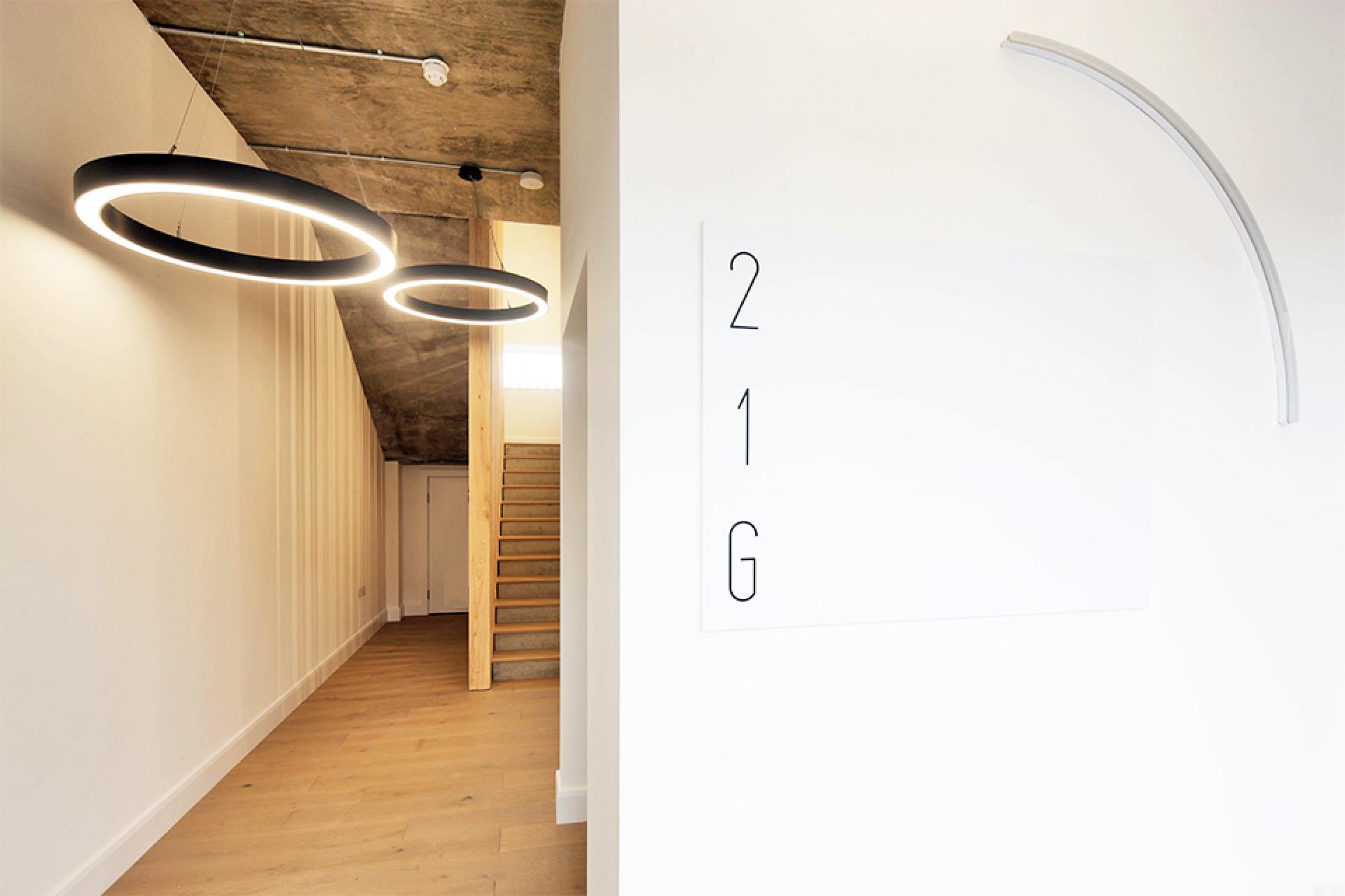 Modern entryway featuring minimalist lighting, natural wood stairs, and sleek signage for an inviting atmosphere.