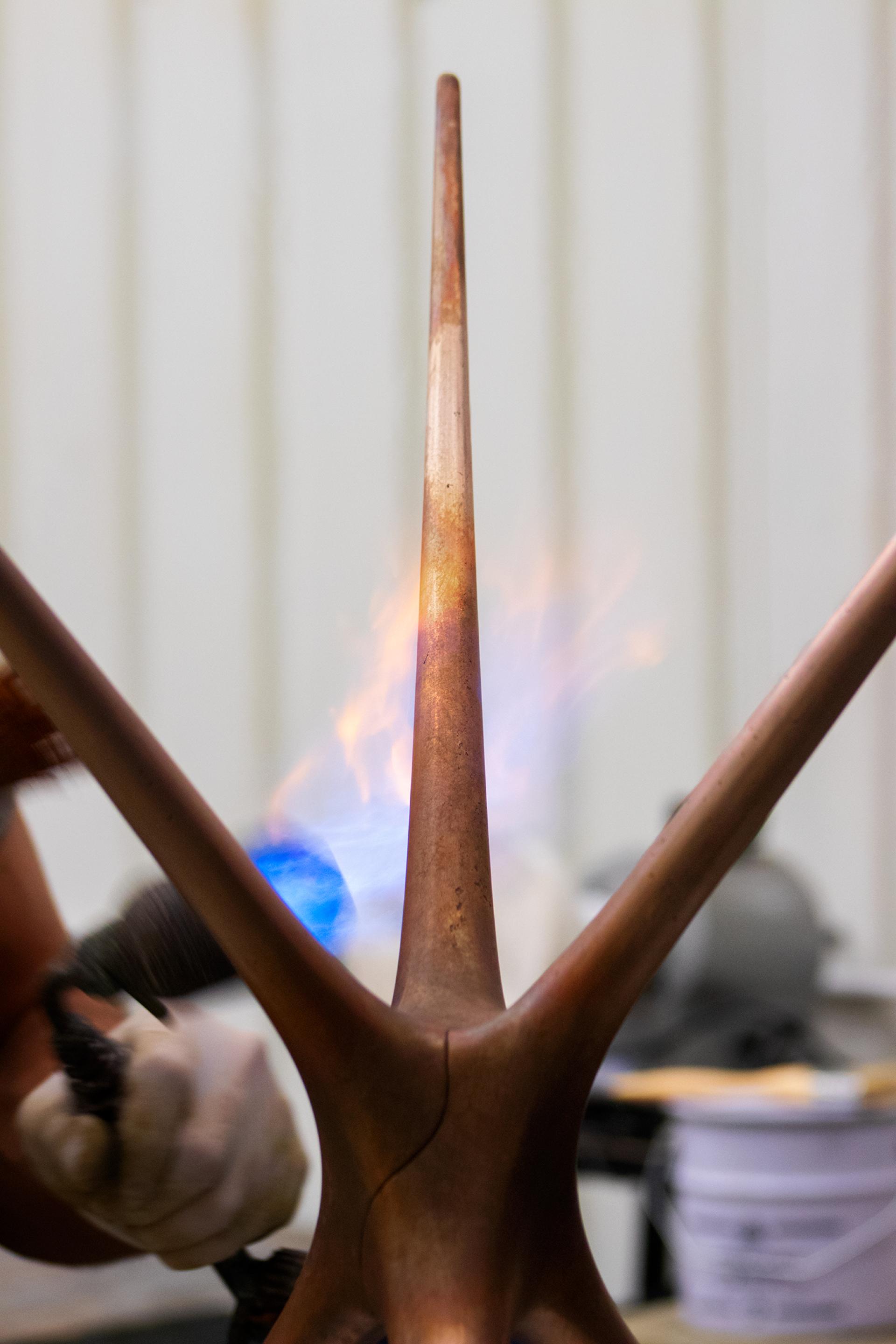 Craftsman shaping the Supernova trestle design, showcasing a flame applied to the metal for finishing touches.