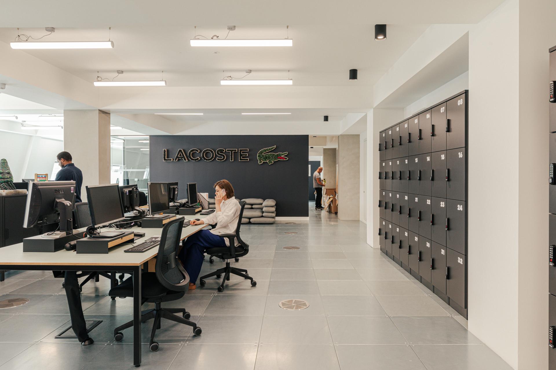 Modern Lacoste workspace featuring sleek desks, computers, and a large logo, reflecting a New York warehouse aesthetic.
