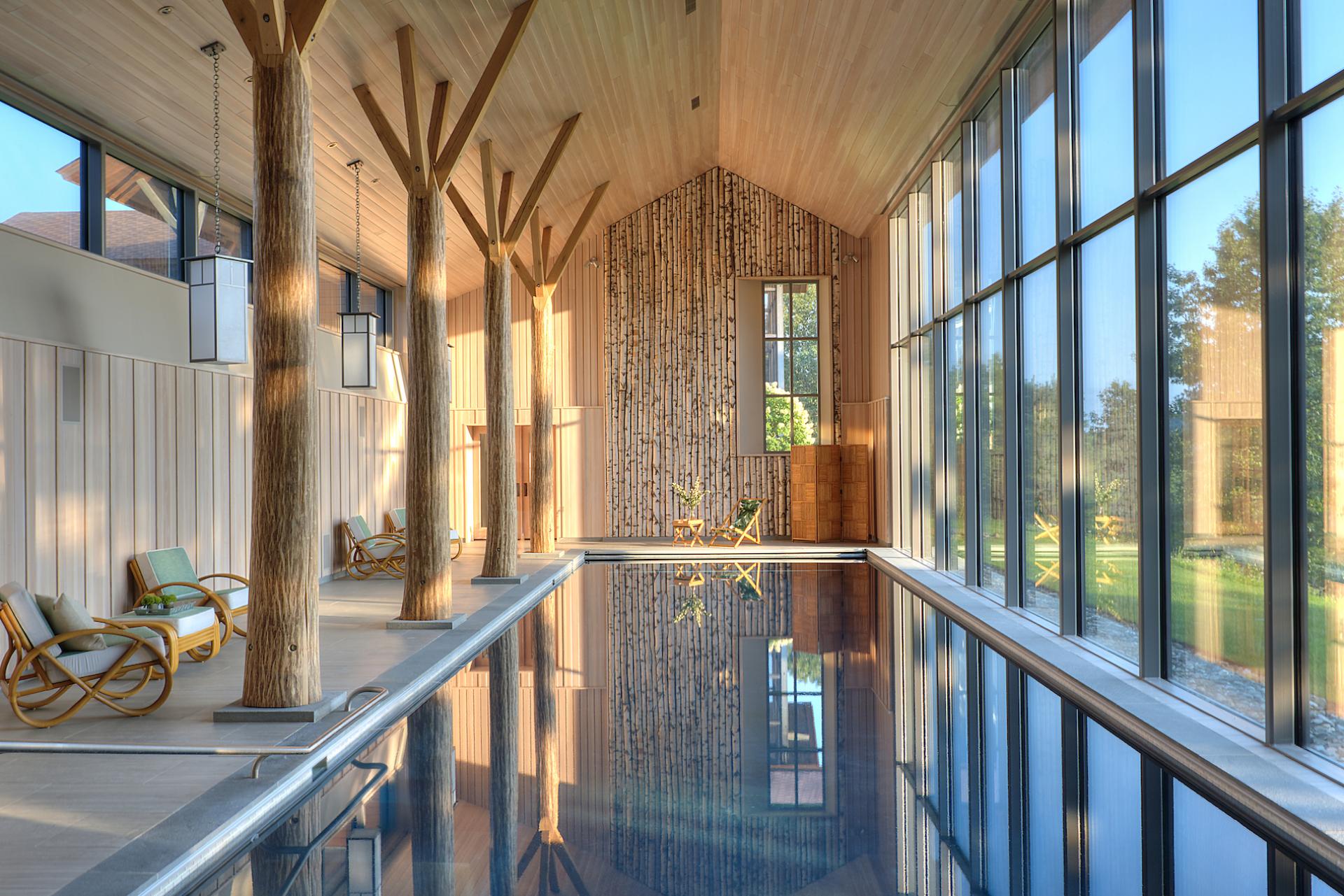 Tranquil interior of Lazy Bear Pool House featuring a reflective swimming pool and tall wooden columns against large windows.