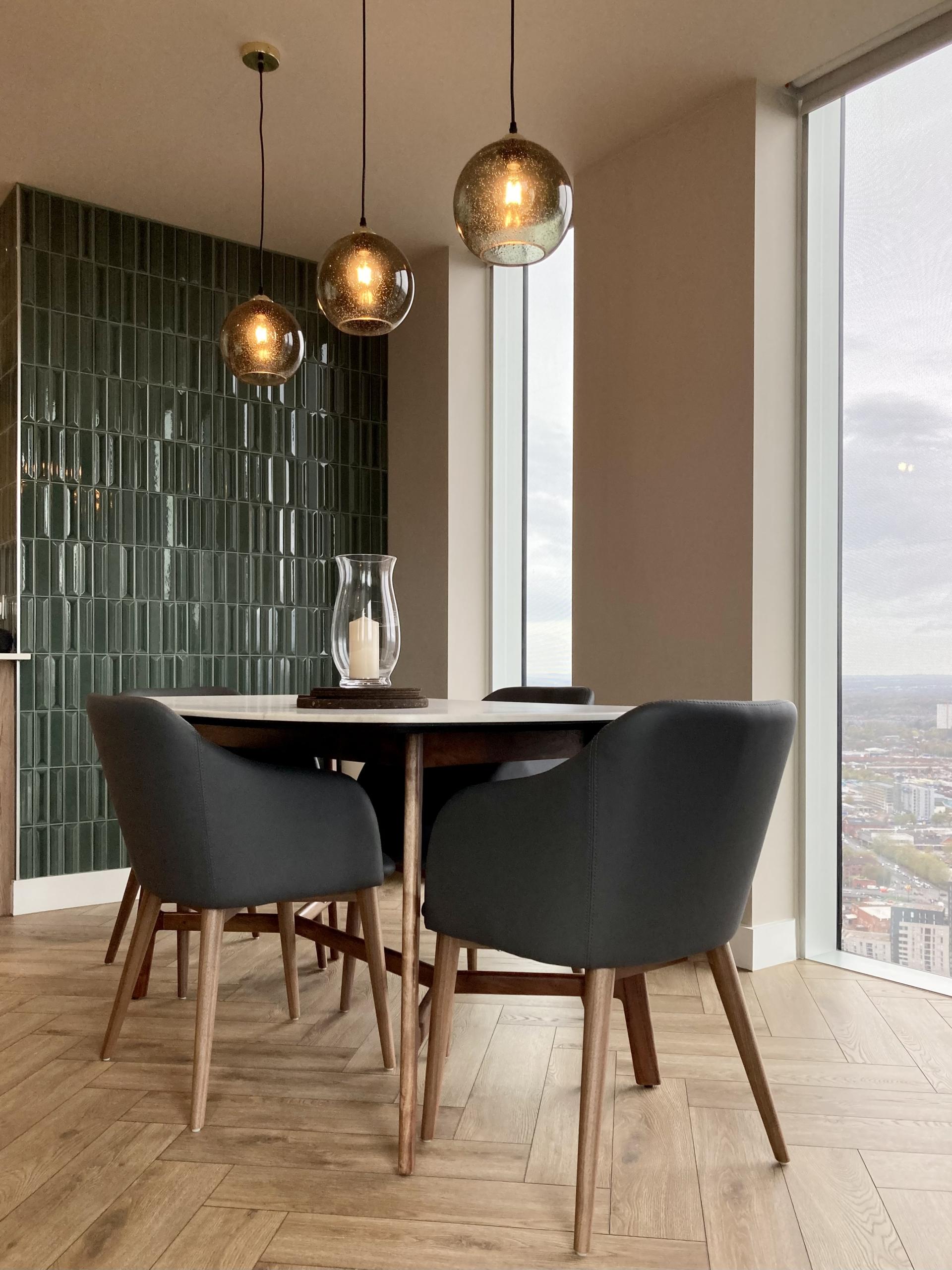 Stylish dining area with modern pendant lighting, wooden table, and elegant chairs overlooking a cityscape, designed by Auric Design.