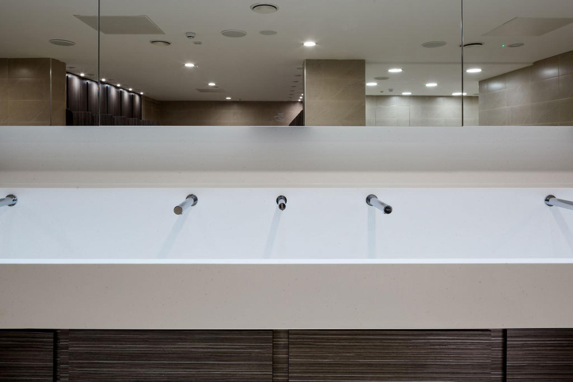 Modern washroom design at Liverpool Street Station featuring sleek white sinks and stylish wooden cabinetry.