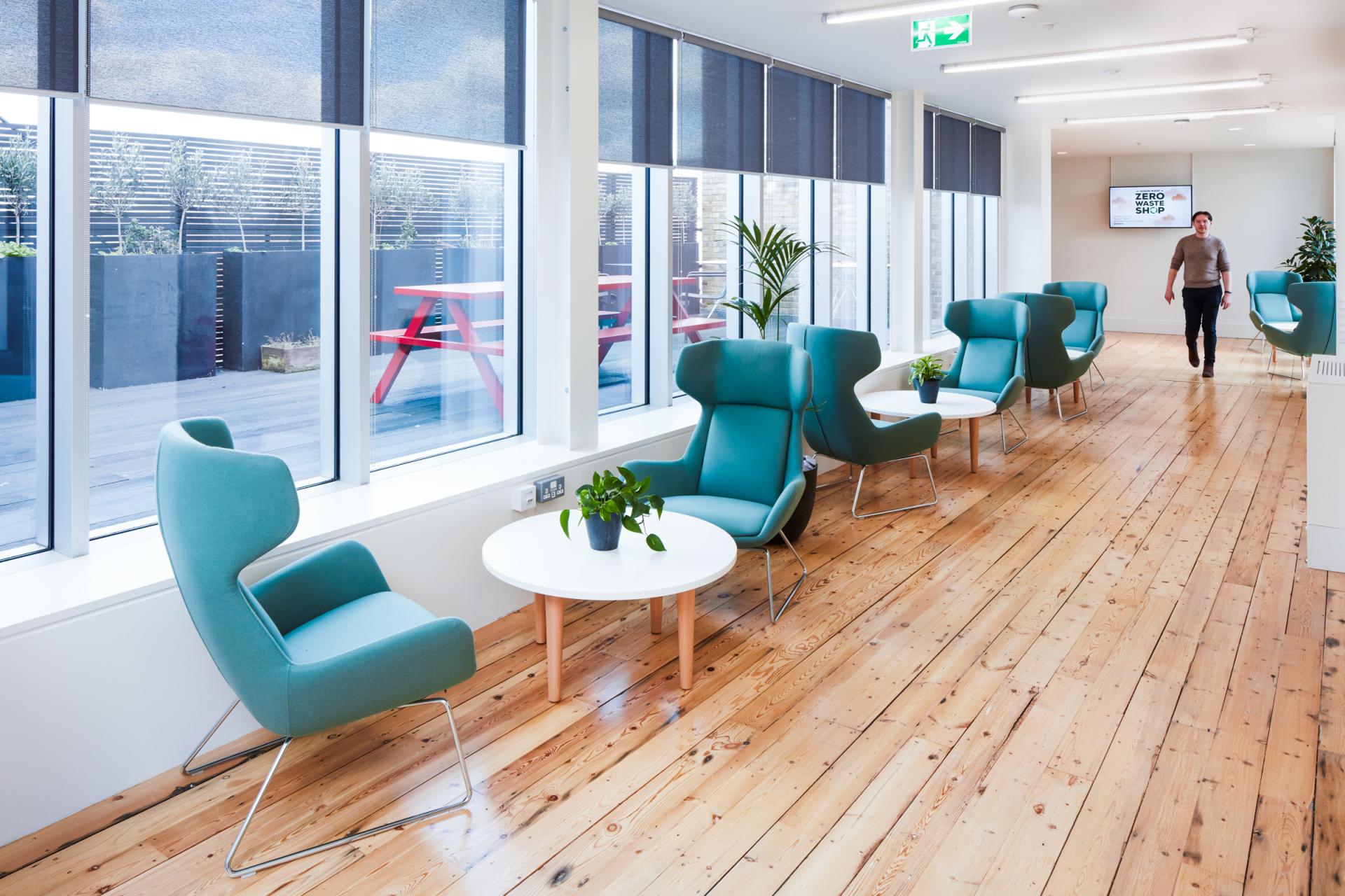 Modern workspace featuring teal chairs, wooden floors, and bright windows, reflecting innovative design at Queen Mary University of London.
