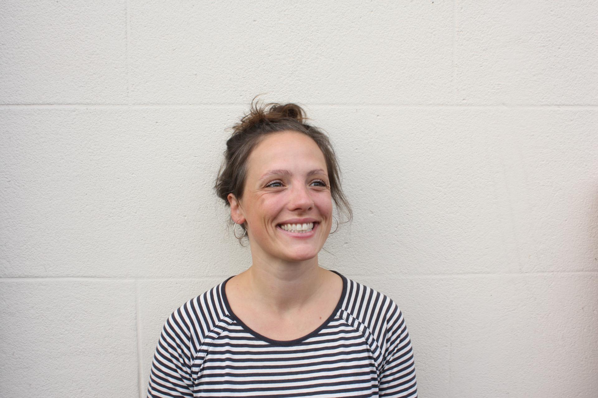 Smiling woman wearing a striped shirt against a white wall, representing the vibrant creative community in Bristol.