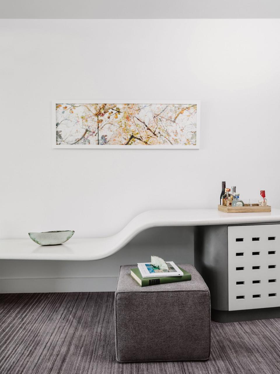 Stylish mid-century hotel interior in Austin featuring flowing white surfaces, a gray ottoman, and nature-inspired artwork.