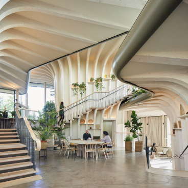 Interior view of Maggie's Leeds, showcasing organic architecture with wooden curves, greenery, and community spaces for emotional support.