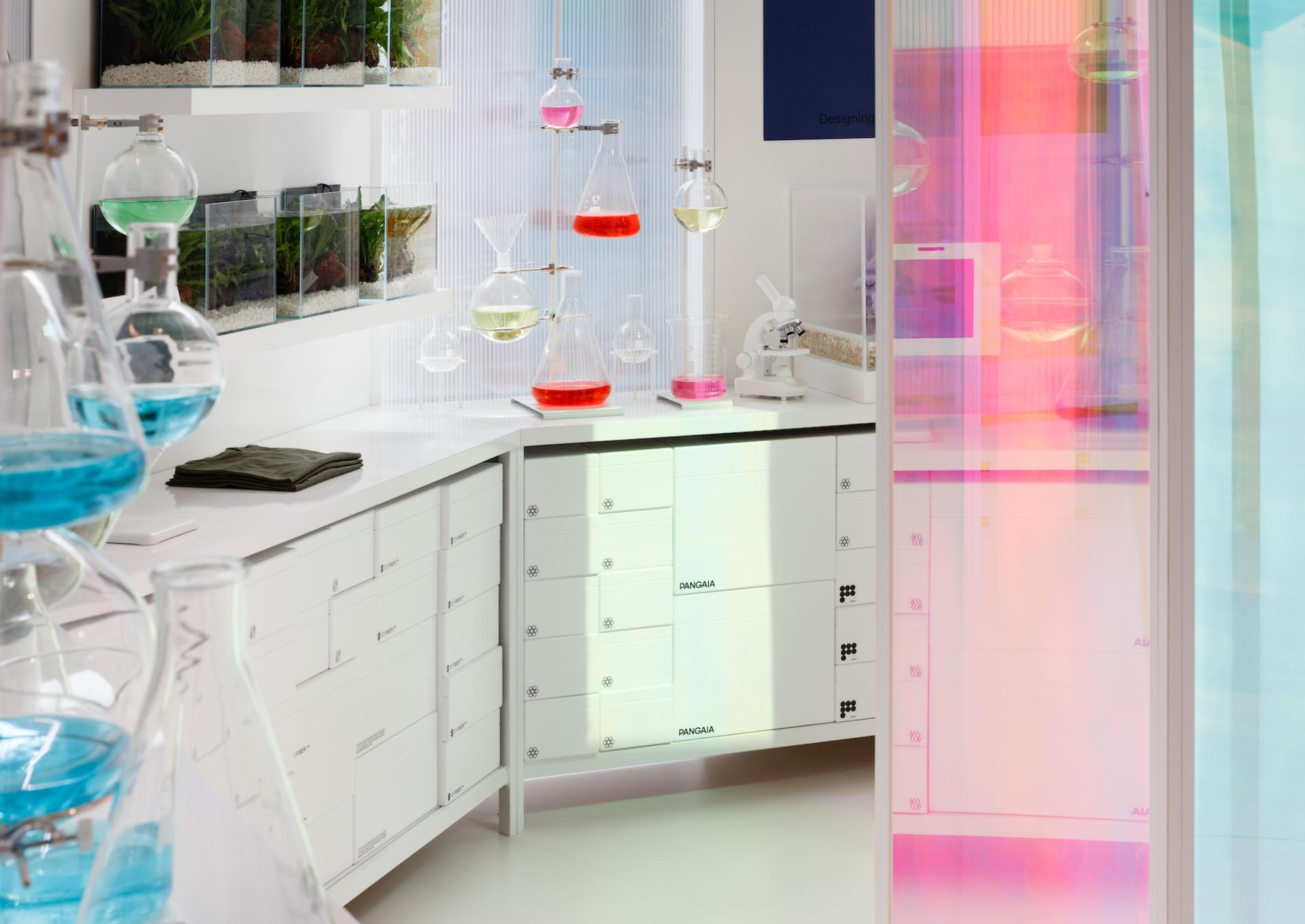 Colorful laboratory setup featuring glassware and vibrant liquids, showcasing Pangaia's eco-conscious design at Selfridges.