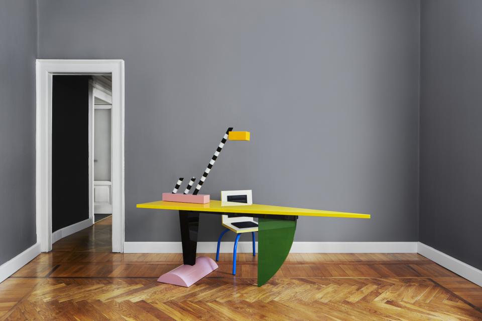 Colorful Memphis Milano desk with a unique lamp, set against a gray wall in a stylish interior.