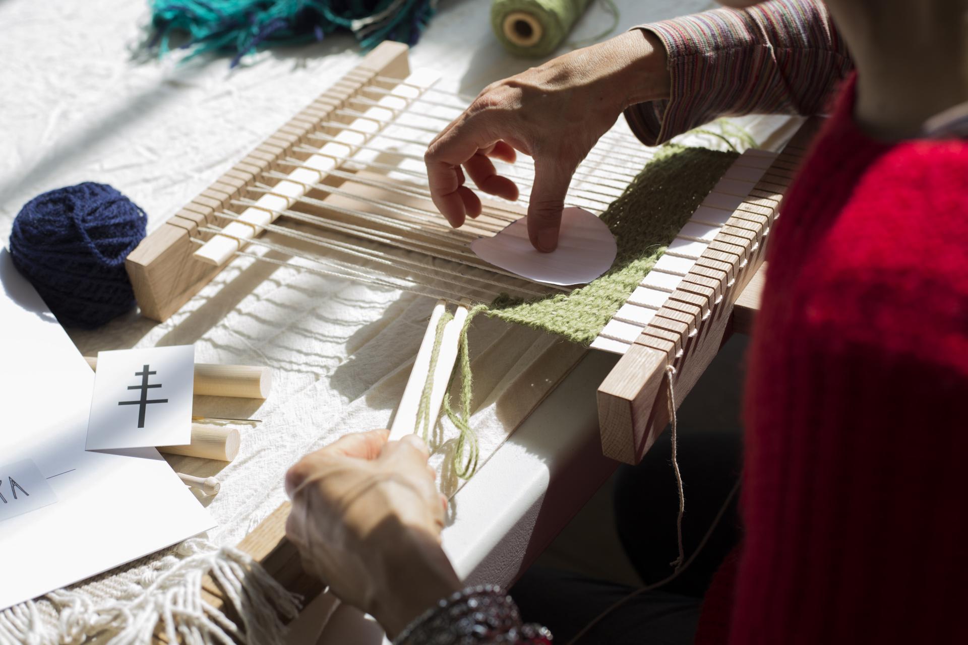 A tapestry weaver's hand working on a loom with colorful yarn and weaving tools, showcasing the art of tapestry creation.