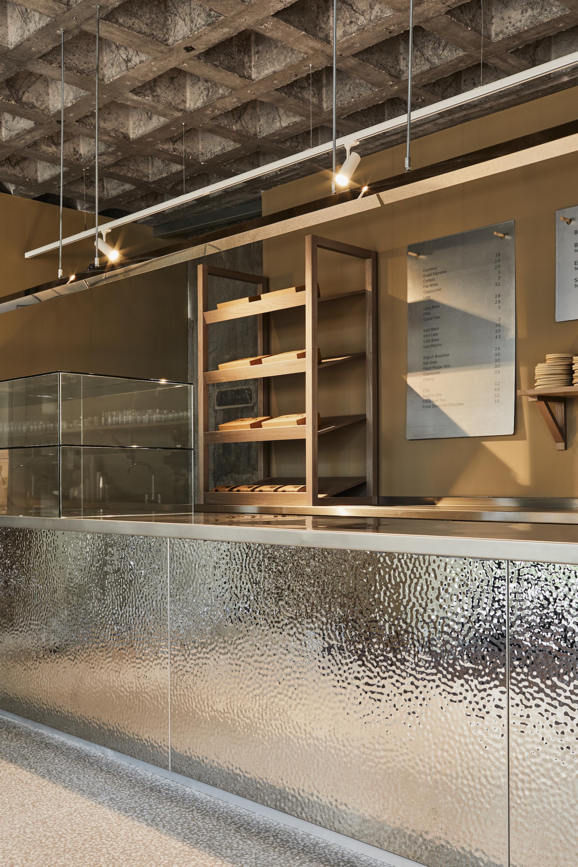 Modern patisserie interior with a sleek counter, wooden shelves, and ambient lighting showcasing Pollen Bakery's heritage and design aesthetics.