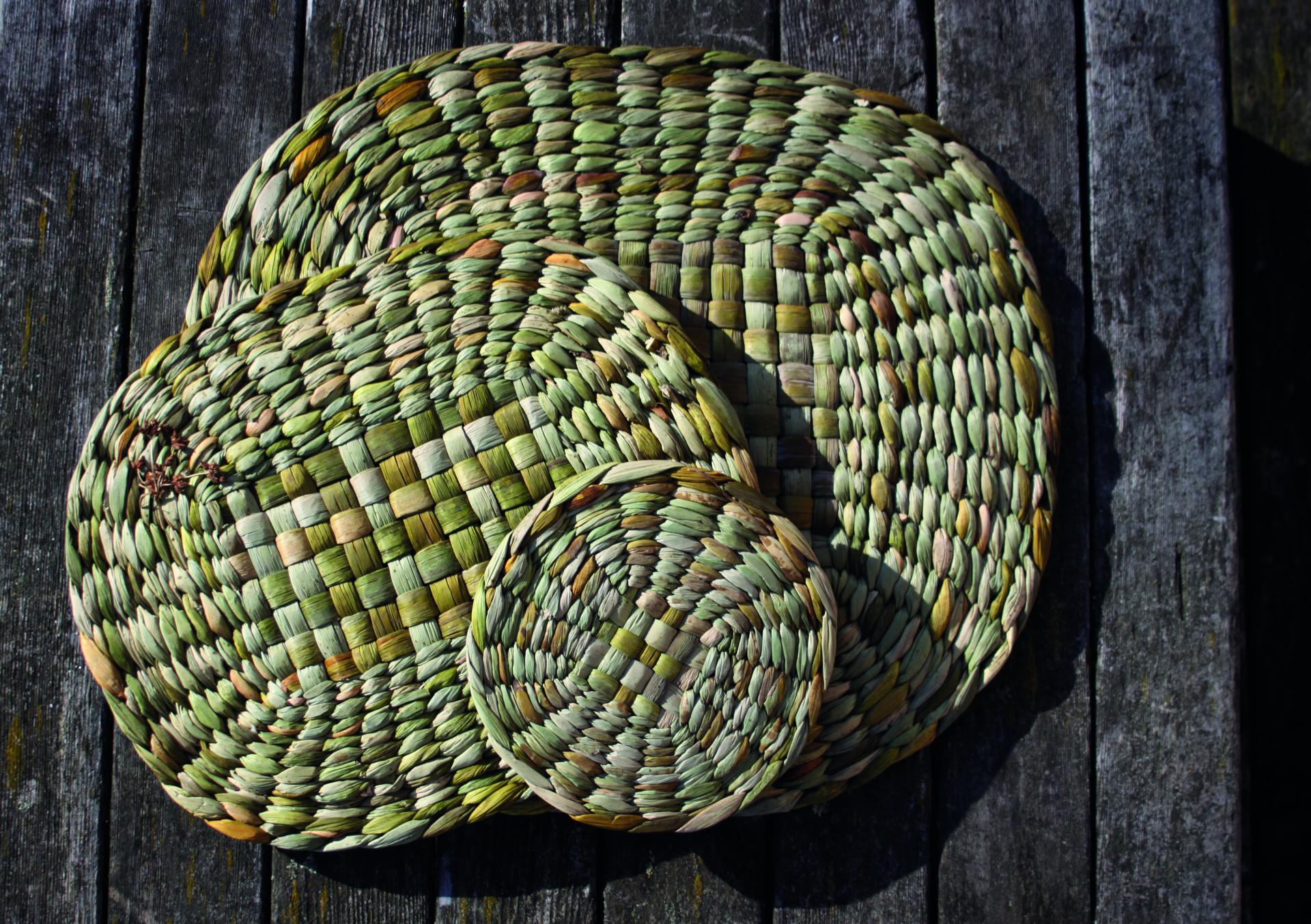 Handwoven green and brown oval and round baskets displayed on a rustic wooden surface, showcasing craftsmanship from London Craft Week 2024.