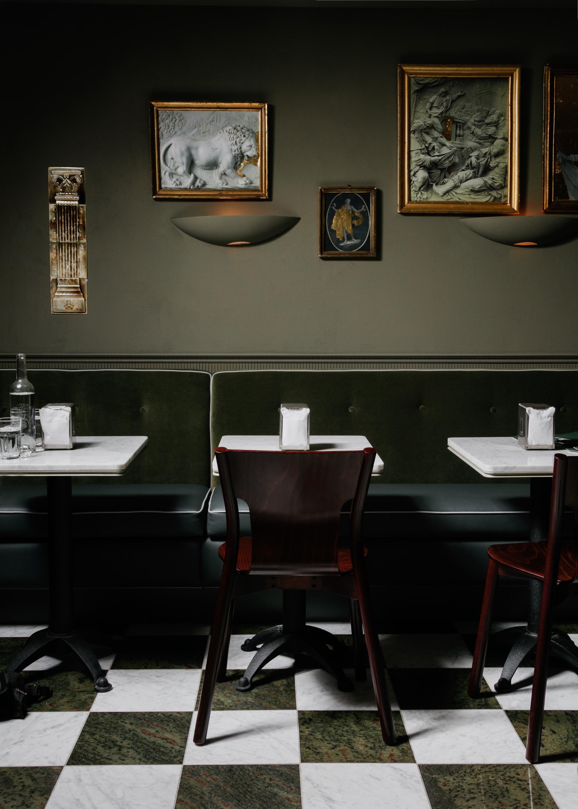 Elegant Italian cafe interior with antique artwork, marble tables, and green upholstery, showcasing a blend of classic and modern design.