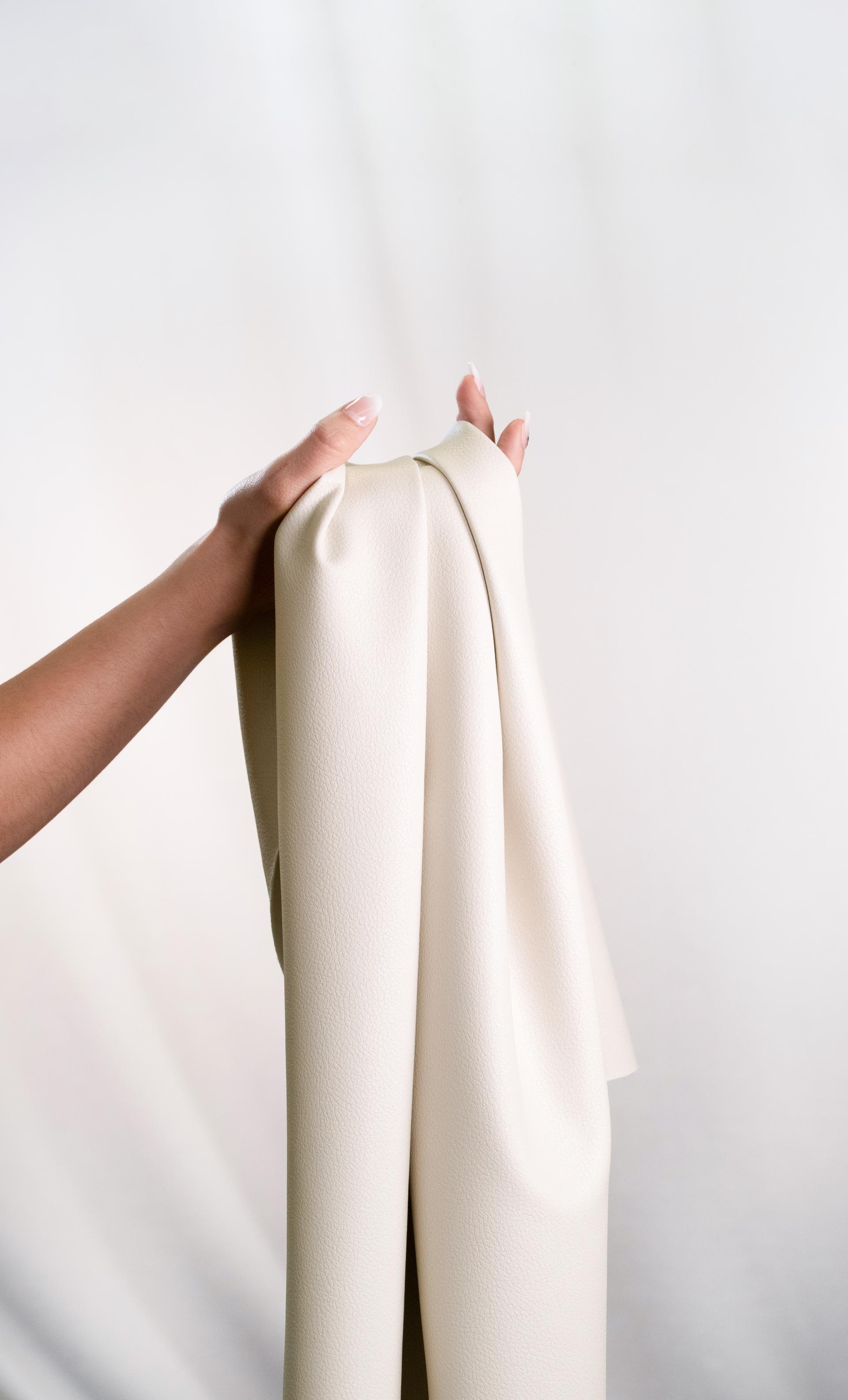 A person holds a soft, cream-colored fabric made from recycled materials, highlighting sustainable textile innovation.