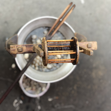 Rustic spinning tool above a pot, highlighting Erez Nevi Pana's process of creating ethical ahimsa silk tapestries.