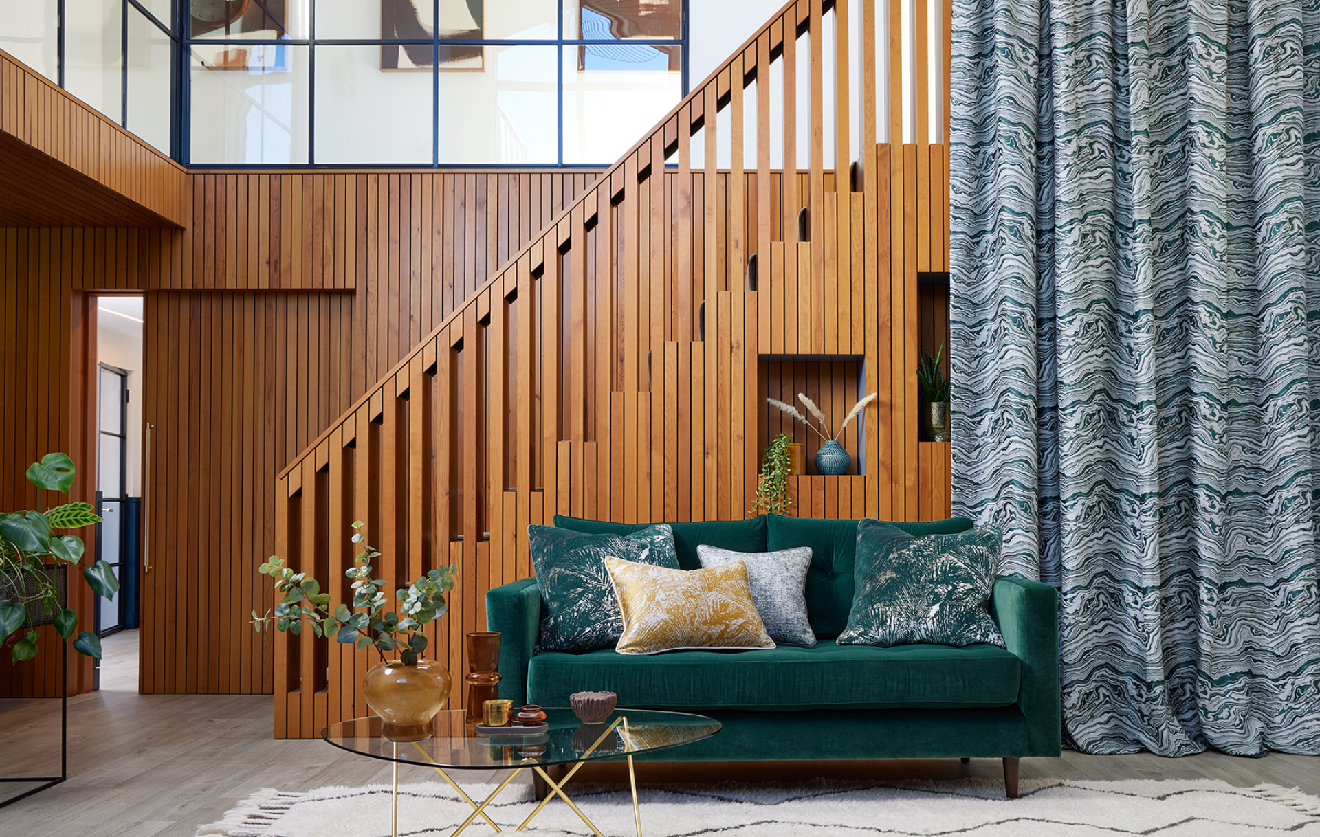Stylish interior scene featuring a green velvet sofa, decorative pillows, wooden staircase, and patterned curtains designed by Panaz.