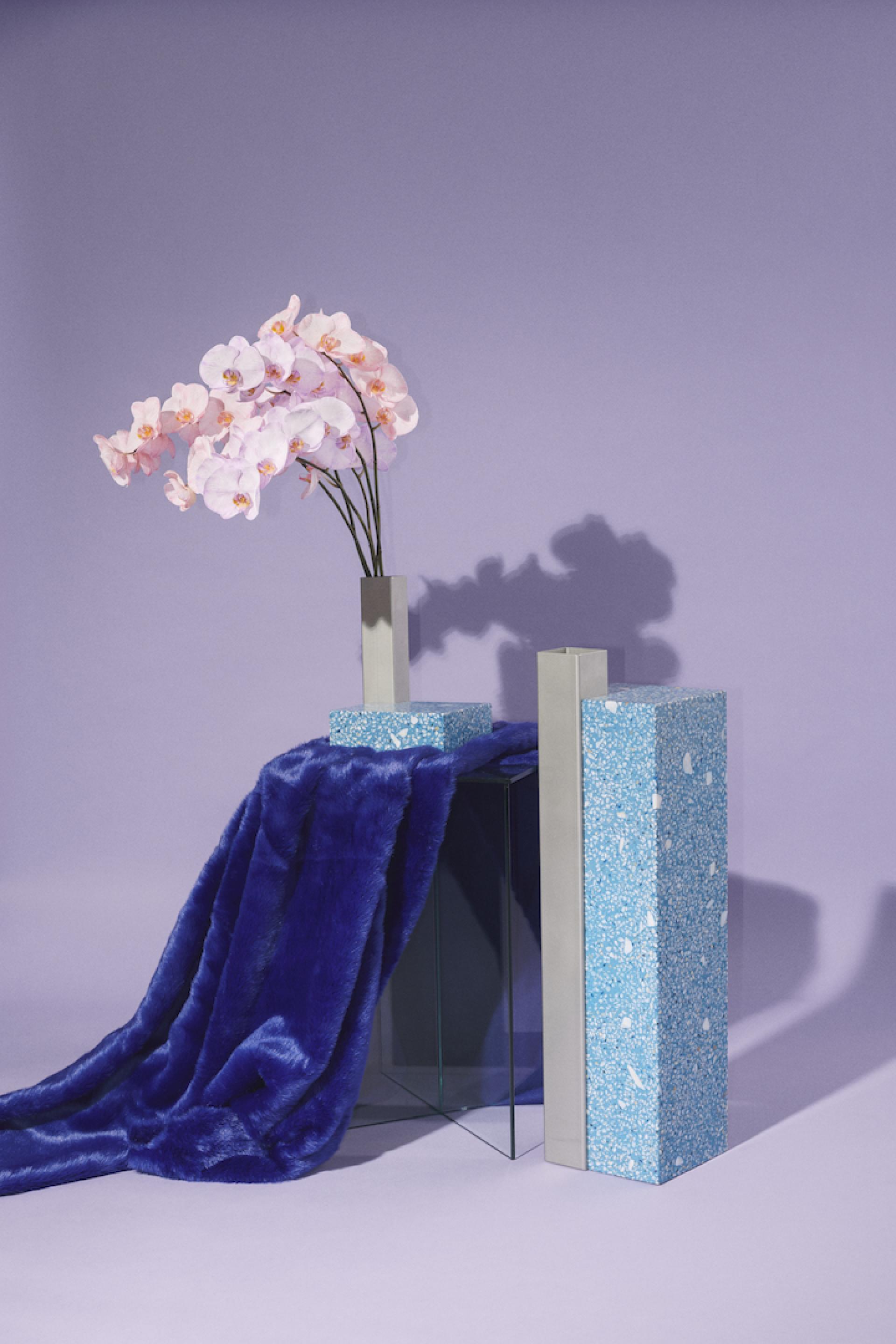 Modern tabletop arrangement featuring pink orchids, blue decorative objects, and a plush purple throw, showcasing Danish design.