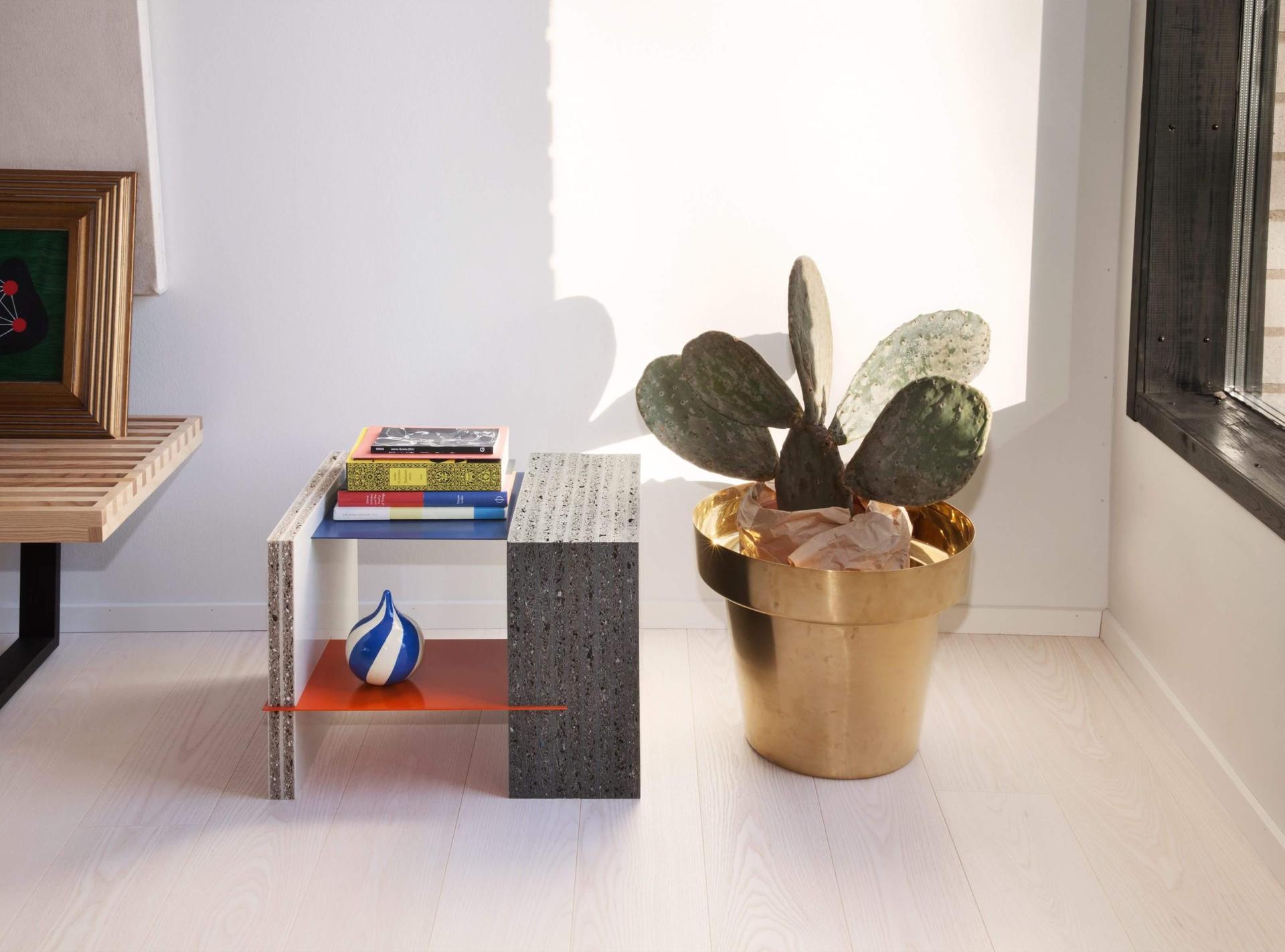 Modern table made from 100% recycled plastic, featuring colorful books, a decorative vase, and a cactus in a gold planter.
