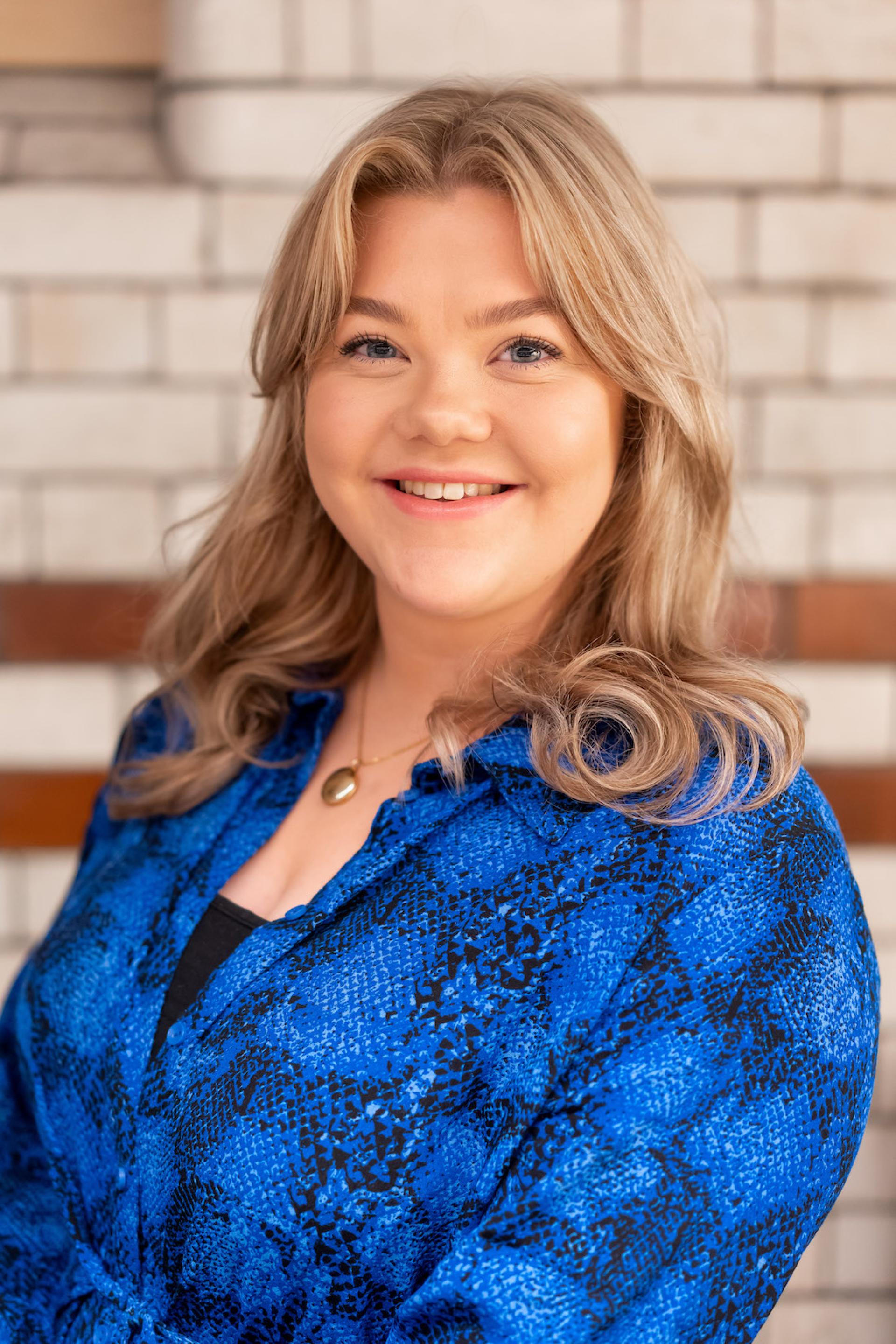 Smiling young woman in a blue patterned blouse, representing discussions on sustainability and value engineering at a seminar.