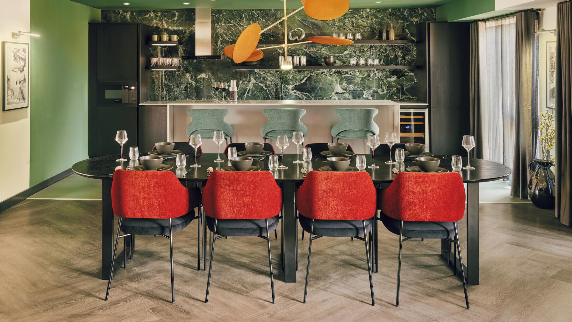 Stylish dining area featuring modern decor, vibrant red chairs, and a green marble kitchen backdrop, highlighting Karndean Commercial and PLATFORM_ collaboration.