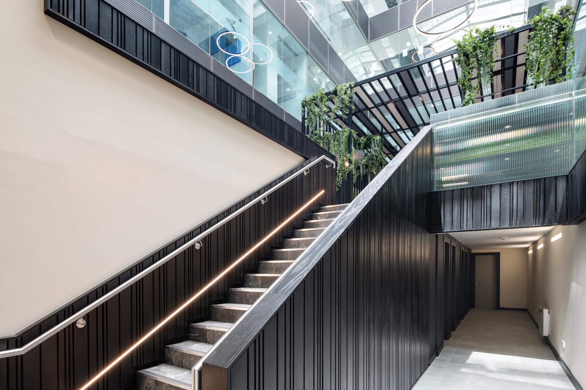Modern staircase design featuring sleek black panels, greenery, and contemporary lighting in One Piccadilly Gardens, Manchester.
