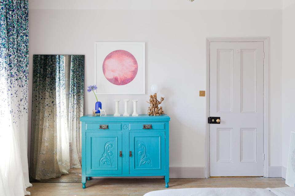 Bright blue cabinet with decorative items, floral accents, and abstract artwork in a stylish interior design space.