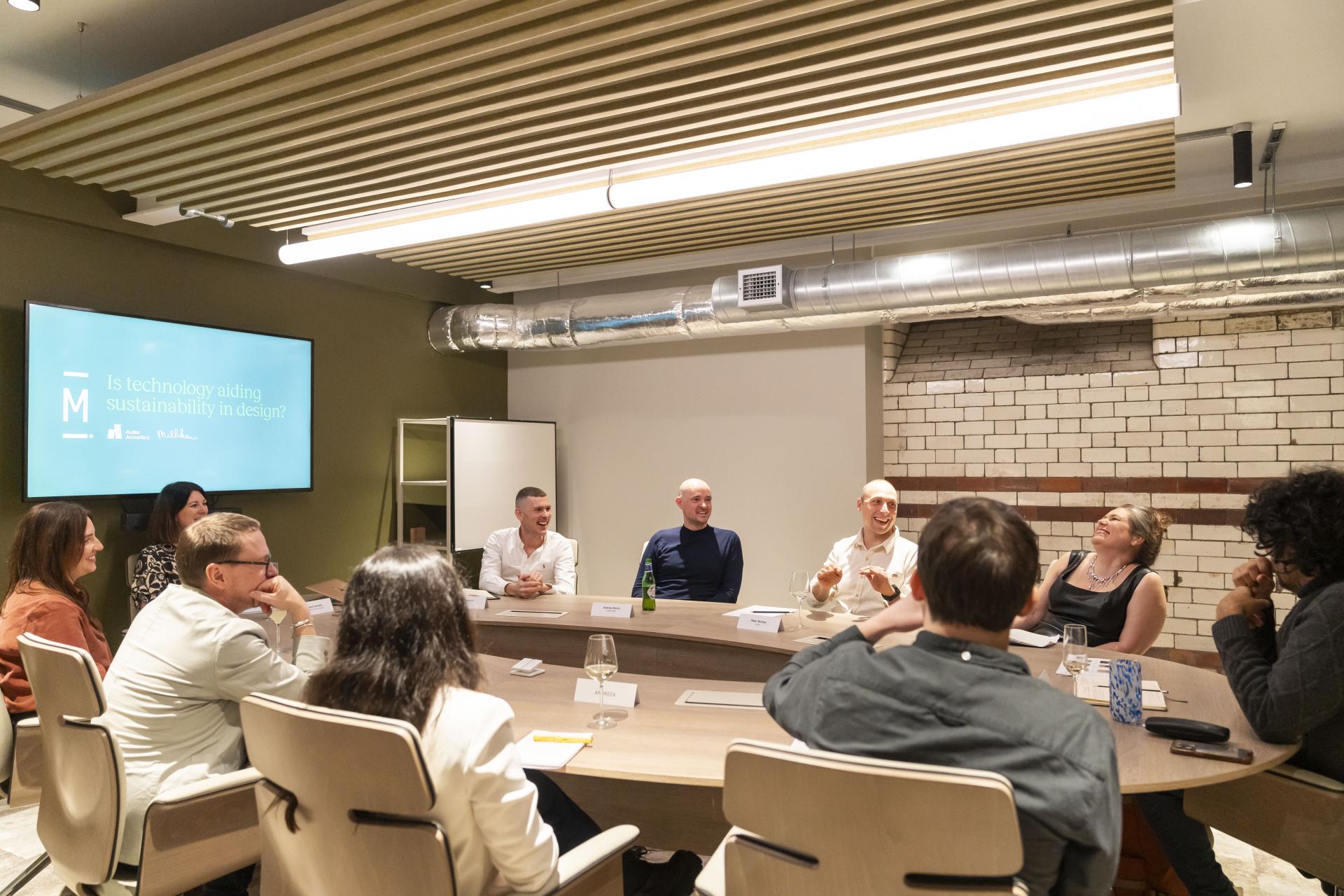 Panel discussion on technology's role in sustainability within design, featuring engaged participants in a modern meeting space.