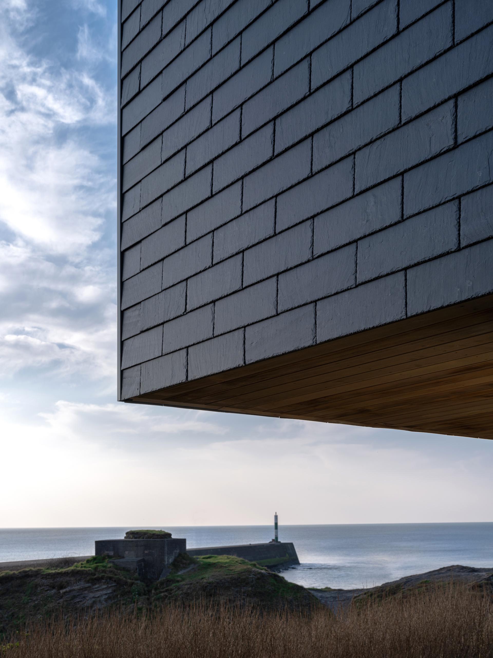Coastal home featuring CUPACLAD 101 Logic slate cladding with a lighthouse in the background against a serene ocean view.