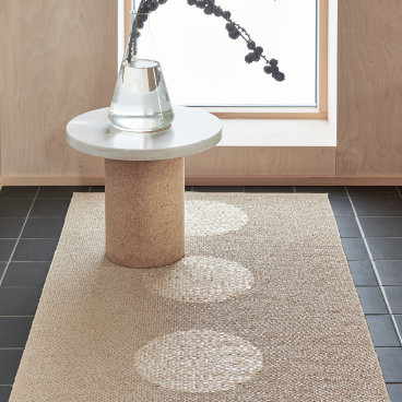 Pappelina's eco-friendly Swedish rug made from BIOVYN™ displayed alongside a minimalist table and floral arrangement.