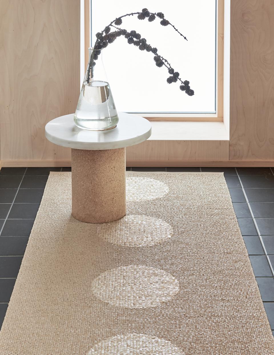 Pappelina's eco-friendly Swedish rug made from BIOVYN™ displayed alongside a minimalist table and floral arrangement.