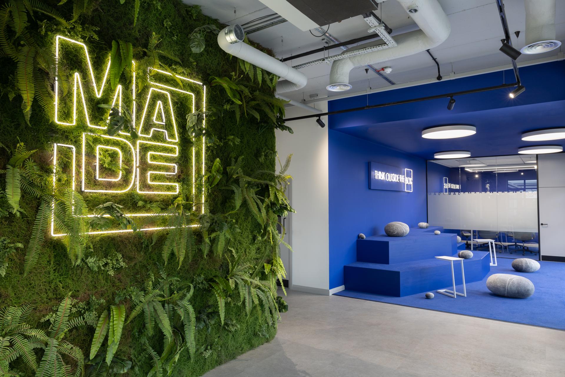 Modern office interior of M1NT Studio featuring lush greenery, a blue accent wall, and creative design elements.