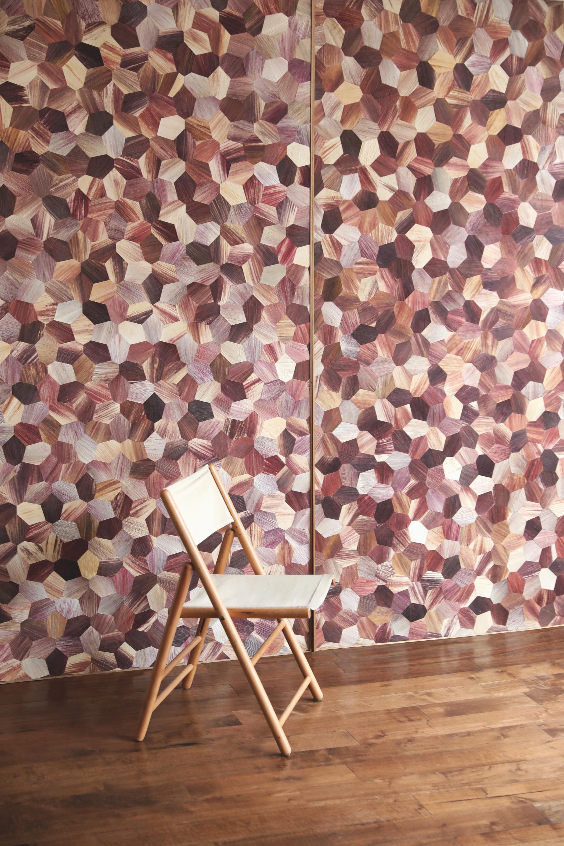 Colorful hexagonal tiles made from Totomoxtle material create a vibrant accent wall behind a simple wooden chair.