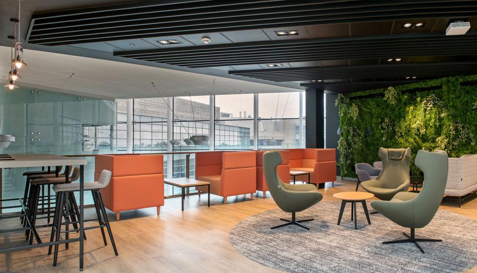 Modern lounge area at Alderley Park featuring colorful seating, a green wall, and large windows for natural light.